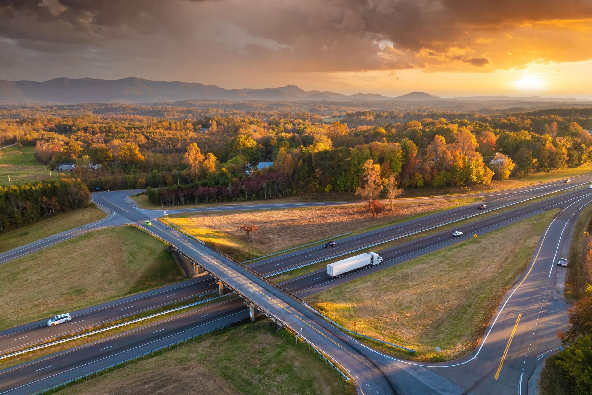Freeway overpass junction with fast moving traffic cars and trucks in American rural area at sunset. Interstate transportation infrastructure in USA